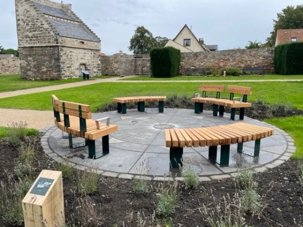 Seating in garden with doocot in background and brass rubbing post in foreground